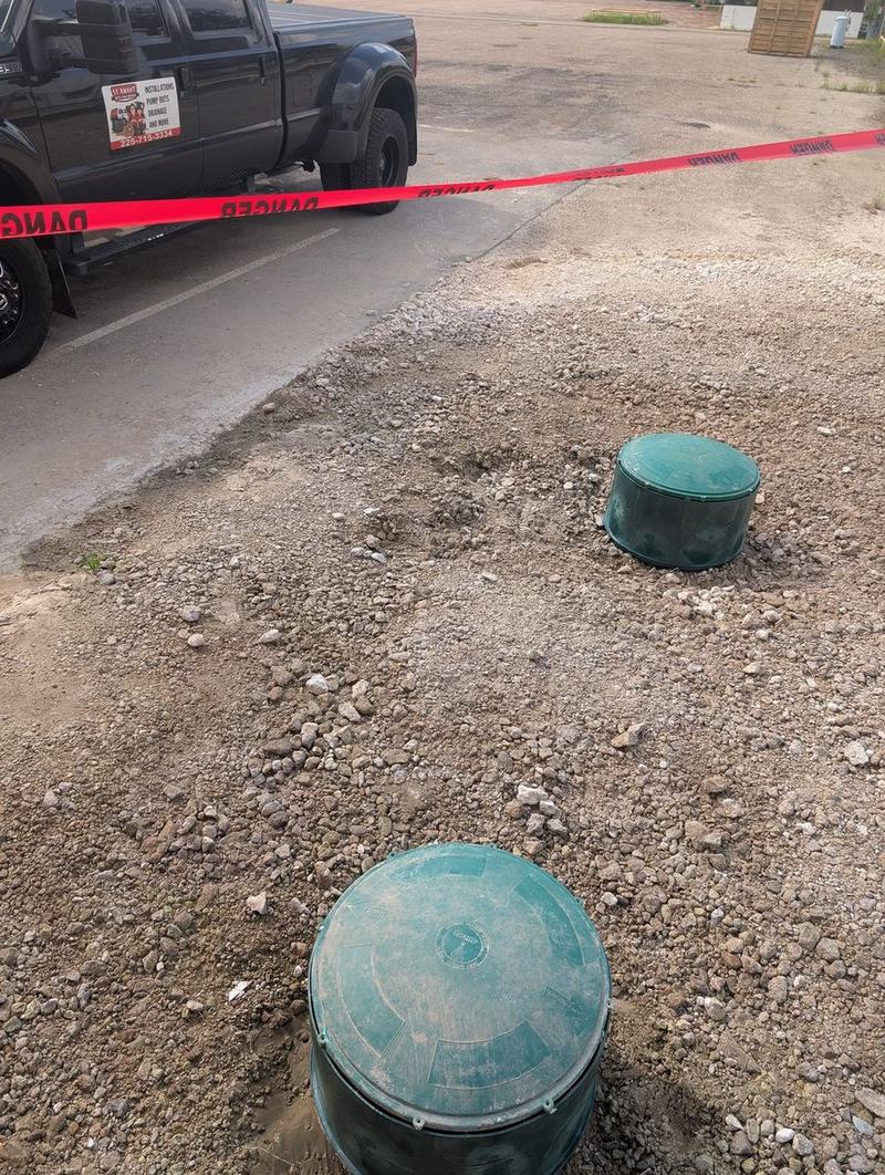 Two green access risers standing in a gravel yard.