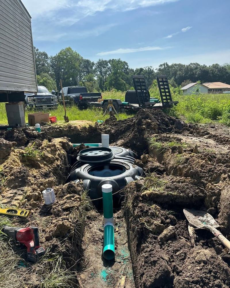 A treatment tank's access risers and lids exposed in a shallow trench.