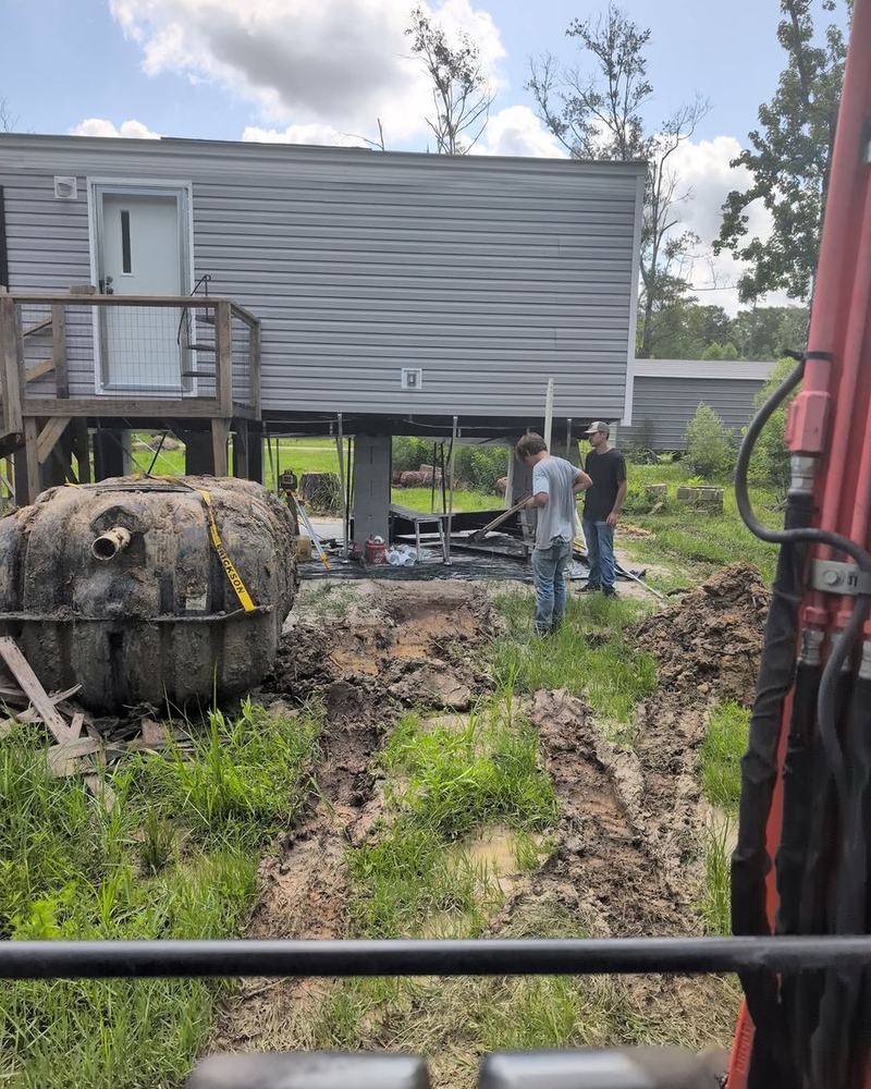 A tank being positioned beside a mobile home on piers.