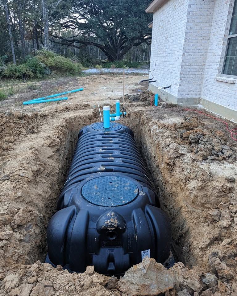 A new treatment tank set in its excavation beside a white brick home.