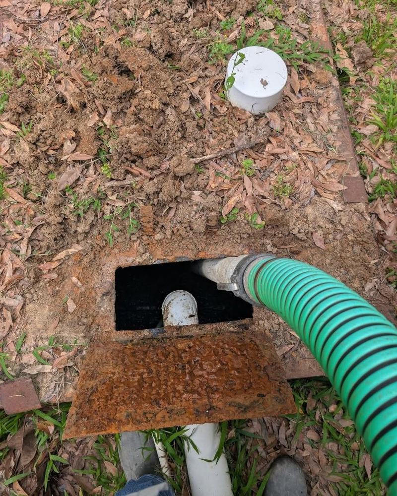 A suction hose feeding through the open access hatch of a septic tank.