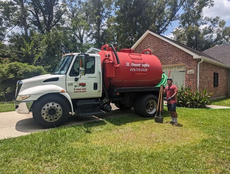 The St. Amant Septic pump truck parked on the lawn of a brick home with a crew member at the hose.